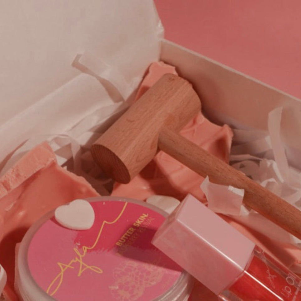 Makeup set with pink container, brush, and other items in a box on a pink background